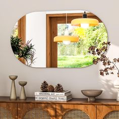 a mirror is hanging on the wall above a table with some plants and vases