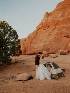 a bride and groom standing next to a tent in front of a large rock formation