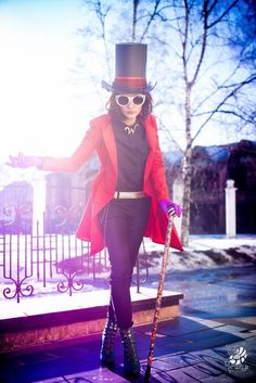 a woman in a top hat and red coat with a cane walking down the street