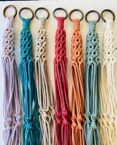 four different colors of rope hanging from hooks on a white wall with metal rings attached to them