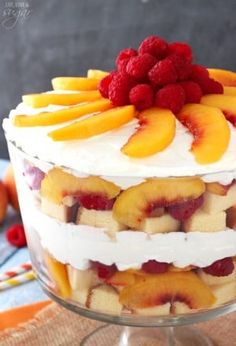 a layered cake with fresh fruit and cream frosting on a glass pedestal, ready to be eaten