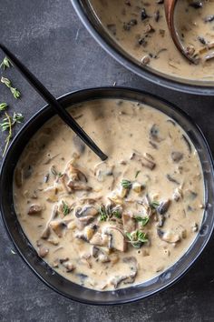 two black bowls filled with mushroom soup on top of a gray table next to a wooden spoon