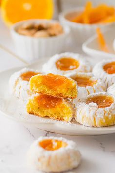 small pastries on a white plate with oranges in the background and powdered sugar around them