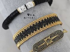 three bracelets with black and gold beaded designs on them, sitting on a gray cloth