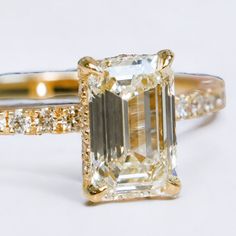 an emerald cut diamond ring with pave diamonds on the sides and gold band around it