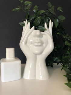 a white vase sitting on top of a table next to a bottle and green plant