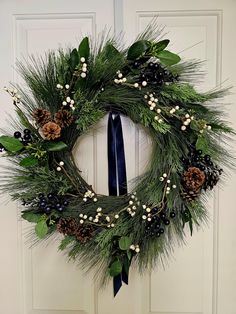 a wreath with pine cones, berries and greenery hangs on the front door doors