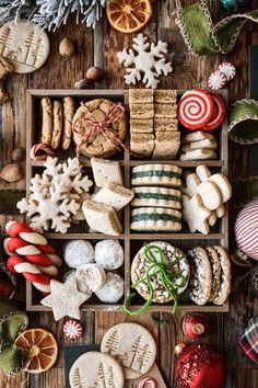 an assortment of christmas cookies and candies on a wooden table with ornaments around them