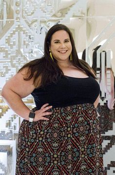 a woman standing in front of a wall with art on it and smiling at the camera