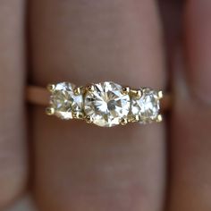 a three stone diamond ring on someone's hand, with the band in yellow gold