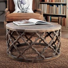 a coffee table with an open book on it in front of a chair and bookshelf