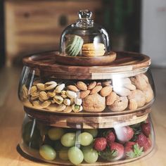 three tiered glass container filled with assorted nuts and fruit on top of a wooden table