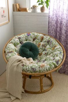 a round chair with a green cushion on it in front of a window and purple curtains