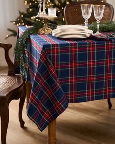 the table is set for christmas with plates and silverware on it, next to a decorated christmas tree