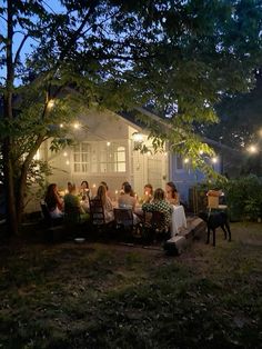 a group of people sitting around a table in front of a white house at night