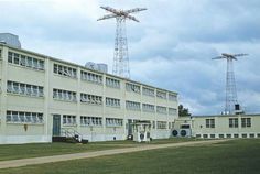 an industrial building with two radio towers in the background and green grass on the ground