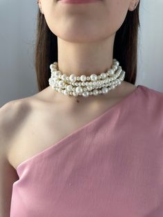 a woman in a pink dress wearing a necklace with white pearls on it's neck