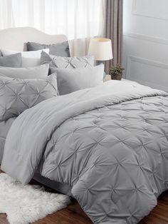 a bed with grey comforter and pillows in a room next to a white rug