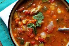 a bowl filled with soup and vegetables on top of a blue table cloth next to a spoon