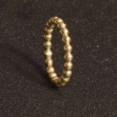 a gold beaded ring sitting on top of a black surface with a small hole in the middle