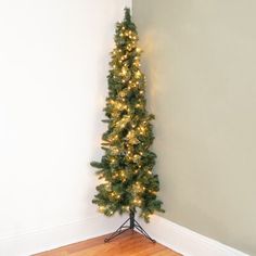 a small christmas tree with lights on it in a corner next to a white wall