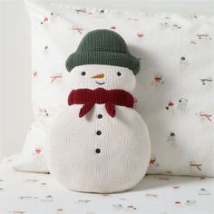 a knitted snowman pillow sitting on top of a bed next to a white pillow