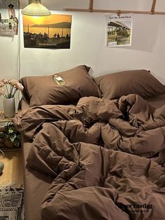 an unmade bed with brown sheets and pillows on the floor next to a lamp