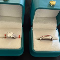 two engagement rings sitting in their boxes on top of each other, one with a diamond and the other without