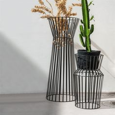 two black vases with plants in them sitting on a white floor next to each other