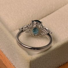 This halo ring features a 7*9mm oval cut London blue topaz and sterling silver finished with rhodium. Customization is available. It is made by hand, and it will take about 7 days to finish the ring after your payment is completed. Main stone: 7*9mm oval cut London blue topaz Main stone weight: Approx 2.00 ct Metal type: sterling silver finished with rhodium Accent stone: cz Customization is available, I also can make it with 14k solid gold (white or yellow or rose) and diamond accent stone, jus London Blue Topaz Ring, Three Stone Ring, Ring Oval, Three Stone Rings, London Blue Topaz, Blue Topaz Ring, Halo Ring, Halo Rings, London Blue