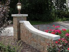 a stone bench sitting next to flowers and a street light on top of a brick wall