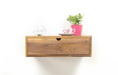 a wooden shelf with some plants and a bowl on it's top, against a white wall