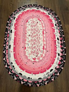 a pink and black round rug on the floor in front of a wooden flooring