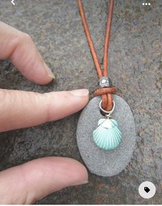 a person holding onto a stone with a shell charm on it's cord necklace