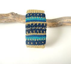 Macrame Bracelet. Cyclades Cuff Bracelet. Greek Islands. Summer. Boho Chic. Gold Shades of Blue. Macrame Jewelry. Gift for her. Adjustable. This is unique exclusive bracelet is handwoven by me in the micro macrame technique. It is carefully thought out and designed to get the desired result. It takes a lot of time, patience and love to knot this bracelet. It is a fine piece of dress jewelry which can be worn from morning to night. Ideal for summer beach parties. It is 3 cm wide and it is made fr Unique Blue Macrame Jewelry, Unique Handmade Blue Bangle, Blue Bohemian Woven Bracelets, Blue Woven Bohemian Bracelets, Unique Hand-wrapped Blue Cuff Bracelet, Unique Hand Wrapped Blue Cuff Bracelet, Unique Blue Bangle Cuff Bracelet, Blue Macrame Beaded Bracelets As A Gift, Bohemian Blue Beaded Bracelets With Rectangular Beads