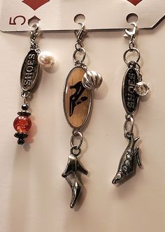 three charms are hanging on a white surface with a red and black tag in the background