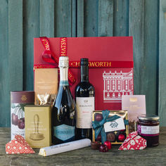 an assortment of wine and chocolates in front of a red gift box on a wooden table