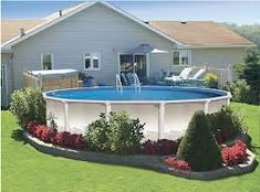 an above ground pool surrounded by shrubs and flowers in front of a house with patio furniture