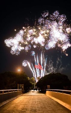 fireworks are lit up in the night sky over a bridge with an american flag on it