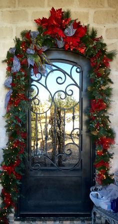 a door decorated with christmas garland and poinsettis is seen through the iron gate