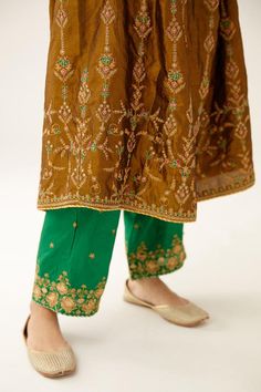 Golden olive silk kurta with contrast piping detailing and dori, thread, beads and sequins embroidery. Comes with green straight pant and a multi-colored silk organza dupatta.
Components: 3
Pattern: Embroidered
Type Of Work: Dori, Thread, Beads, Sequins
Neckline: V Neck
Sleeve Type: Three quarter
Fabric: Silk, Dupatta: Silk organza, Lining: Fine cotton
Color: Gold,Brown
Other Details: 
Attached lining
Occasion: Mehendi and Haldi - Aza Fashions Silk Sets With Resham Embroidery And Straight Pants, Silk Palazzo Set With Dupatta, Bollywood Style Tussar Silk Palazzo Set With Embroidered Border, Festive Embroidered Border Pants For Diwali, Festive Wedding Pants With Embroidered Border, Festive Silk Palazzo Set With Embroidered Border, Festive Silk Pants With Zari Work, Traditional Silk Pants With Zari Work, Designer Silk Sharara With Embroidered Border