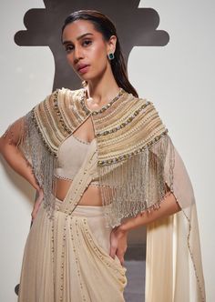 Embodying strength and style, our Tatiana sari set seamlessly combines effortless silhouettes, elegant drapery, delicate embroidery, and distinctive fringe details to create a look that is both soft and resilient. Festive Embellished Pre-draped Saree, Silk Pre-draped Saree With Cape Sleeves And Zari Work, Evening Pre-draped Saree With Resham Embroidery And Cape Sleeves, Pre-draped Set With Sheer Dupatta For Reception, Traditional Drape Sets With Tassels For Eid, Pre-draped Sets For Reception With Traditional Drape, Pre-draped Traditional Sets For Reception, Festive Pre-draped Set With Sheer Dupatta, Designer Floor-length Sets With Tassels