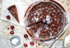 a cherry tart pie with one slice cut out and cherries on the side