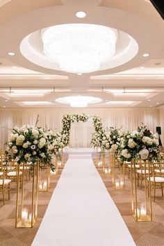 the aisle is lined with gold chairs and white flowers in vases on each side