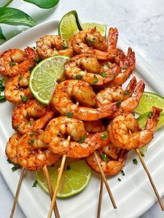 shrimp skewers with lime wedges on a white platter next to sliced lime