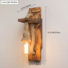 a wooden light fixture with rope hanging from it's side and an electric bulb attached to the wall