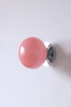 a pink door knob on a white wall with a light bulb in the middle and an orange ball at the top