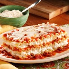 a white plate topped with lasagna covered in sauce and cheese next to a bowl of rice