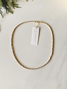 a gold necklace with a white tag hanging from it's side on a marble surface