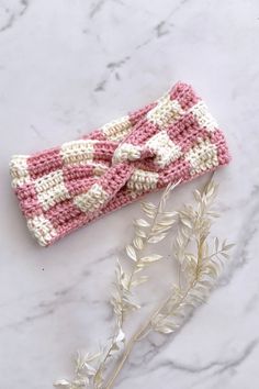 a pink and white knitted headband with a bow sitting on top of a marble surface